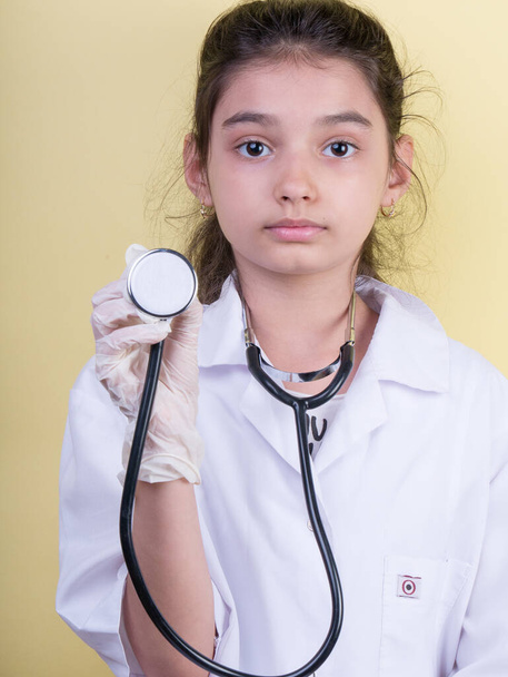 先生の制服を着ている間に聴診器を装着したアジアの女医。背景色の上に隔離されて立つ。COVID-19。隔離だ。女の子は医者を演じる。教育と職業概念は - 写真・画像