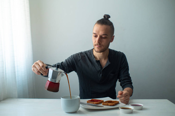 Hombre rubio caucásico sirviendo café en el desayuno sobre una mesa blanca - Foto, imagen