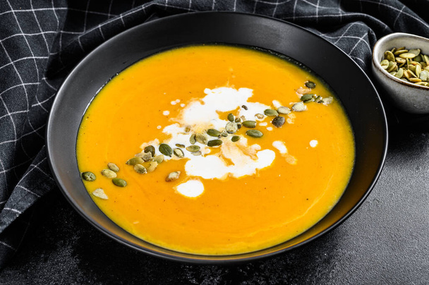 Pumpkin cream soup with cream and pumpkin seeds. black background. Top view. - Photo, Image