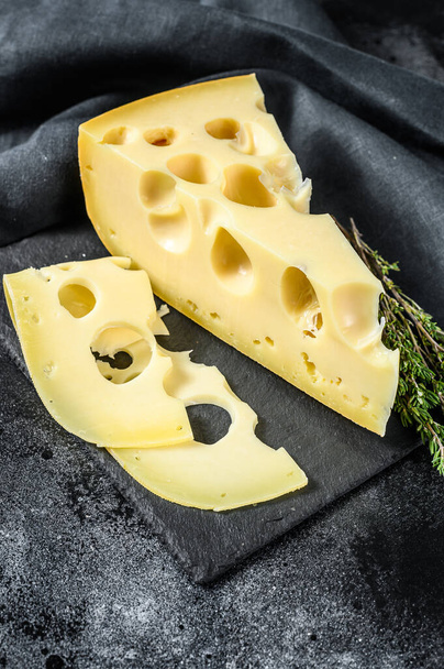 Egy darab maasdami sajt nagy lyukakkal. Fekete háttér. Felülnézet. - Fotó, kép