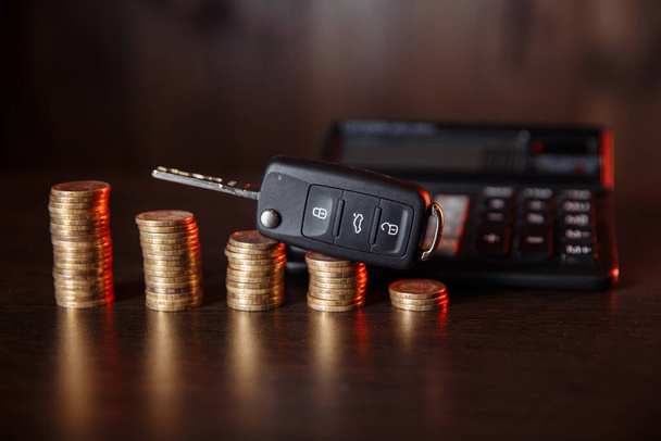 Egy halom érme és számológép fekete autó kulccsal az asztalon - Fotó, kép