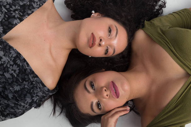 face of two young brunette women with makeup, lying on the floor facing forward, one with afro hair the other with straight hair - Photo, Image
