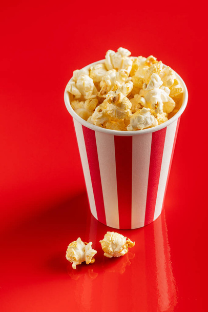 Sweet popcorn in striped paper cup on red background. - Foto, Bild