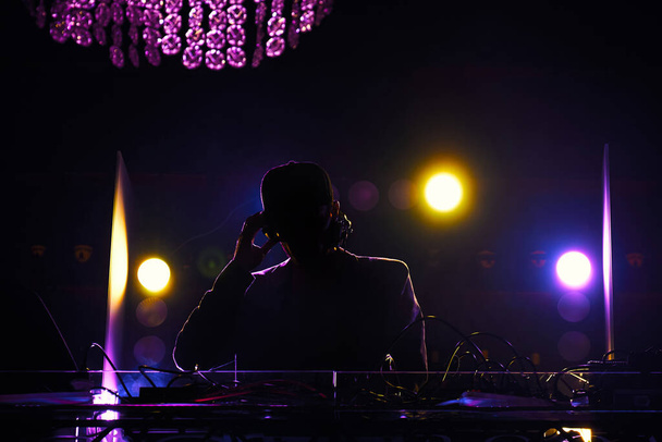 A disc jockey at the turntable. DJ mixing tracks on a mixer in a nightclub.DJ silhouette over foggy illuminated background. - Photo, image