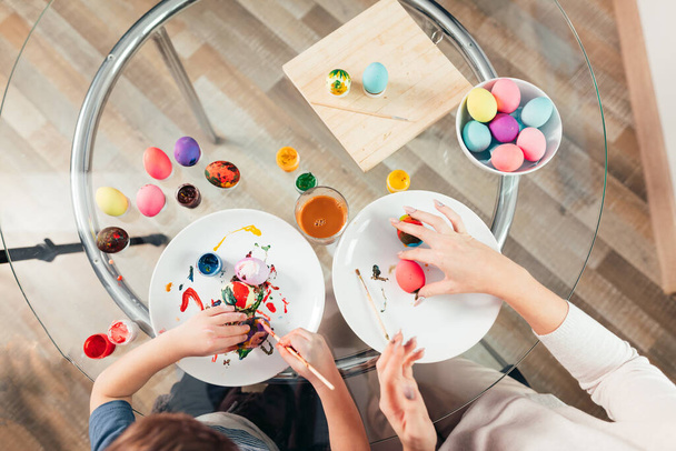 Top view of woman and child painting Easter eggs over wooden background - Foto, immagini