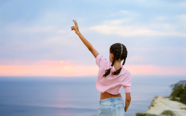 A girl in a pink T-shirt stands with her hand held high on the e - Photo, Image