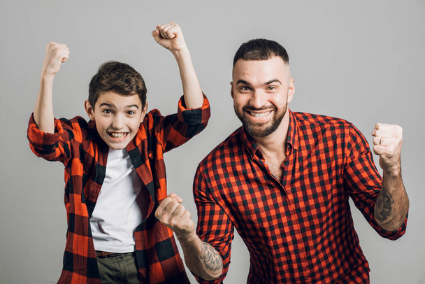 a cheerful young man and his son shouting with arms raised in success - Foto, afbeelding