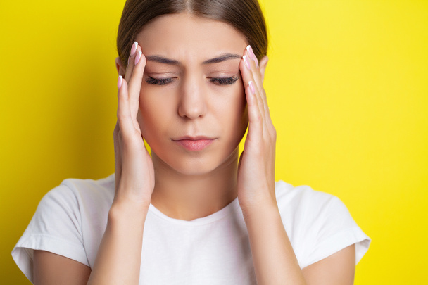 Een jonge vrouw houdt haar hand tegen haar hoofd en voelt een ernstige hoofdpijn - Foto, afbeelding