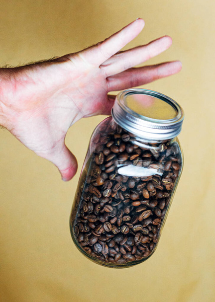 Рука зі скляним горщиком, повним кавових зерен
 - Фото, зображення