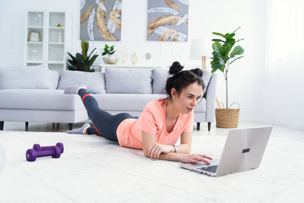 Young pretty woman trains at home online with elastic bands for fitness. - Foto, Bild