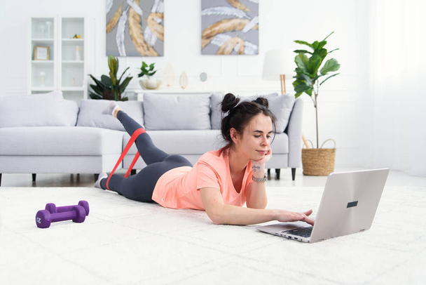 Young pretty woman trains at home online with elastic bands for fitness. - Foto, immagini