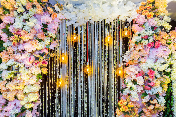 Πολύχρωμα τεχνητά λουλούδια με διακοσμητικά αντίκες Έντισον στυλ λαμπτήρων πυράκτωσης κρέμονται στη διακόσμηση σκηνή του γάμου. - Φωτογραφία, εικόνα