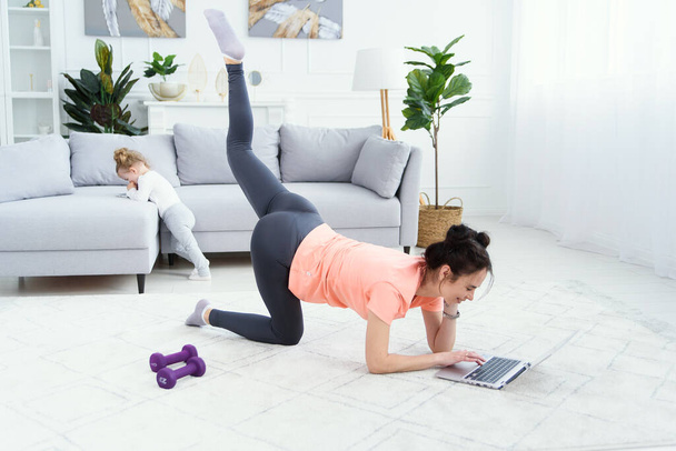 Fitness woman exercising on the floor at home and watching fitness videos in a laptop. Pretty girl doing online fitness workout. - Fotó, kép