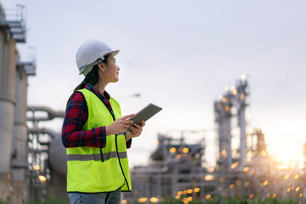Asian woman petrochemical engineer working with digital tablet Inside oil and gas refinery plant industry factory for inspector safety quality control - Photo, Image