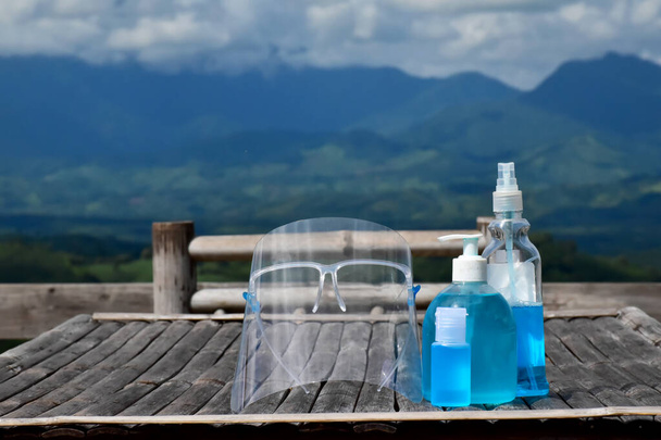 Medizinische Ausrüstung, Gesichtsschutz, Händedesinfektionsmittel und Alkohol-Gel auf dem Tisch mit verschwommenem Hintergrund der Berge dahinter. Konzept zum Schutz des Coronavirus, das sich jetzt weltweit ausbreitet. - Foto, Bild