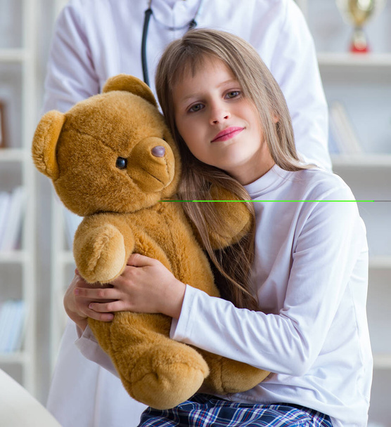 Женщина-врач осматривает маленькую симпатичную девочку с игрушечным мишкой - Фото, изображение