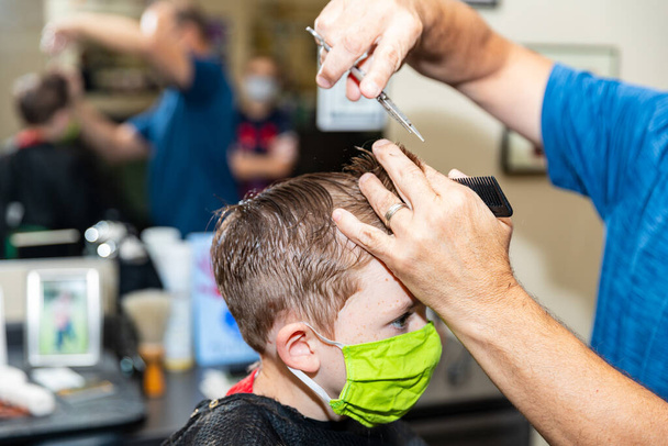 Jongen krijgt kapsel tijdens pandemie tijdens het dragen van gezichtsmasker - Foto, afbeelding