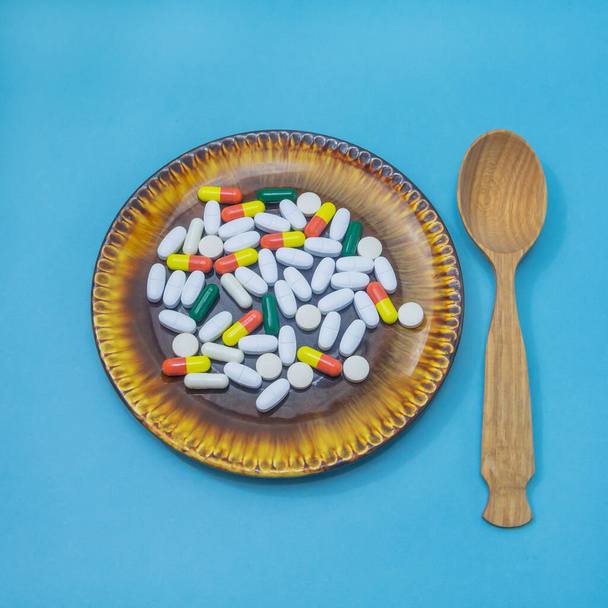 Medication pills and capsules on plate and spoon. Blue background, square size. Medicine, pharmacy, treatment concept. - Foto, afbeelding