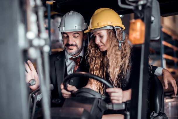 Engineer woman driving forklift and businessman wearing a hardhat standing at goods warehouse cargo and check for control loading from Cargo freight ship for import and export. Teamwork concept  - Photo, Image