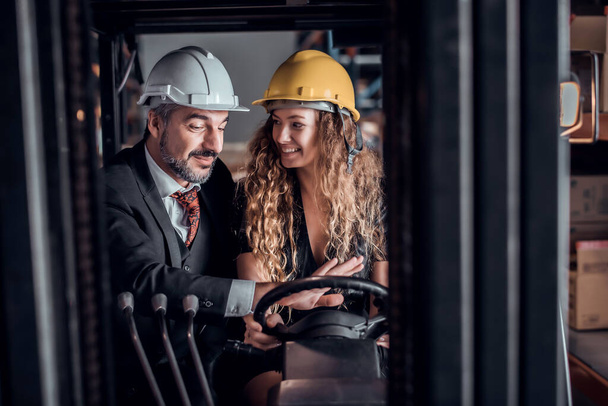 Engineer woman driving forklift and businessman wearing a hardhat standing at goods warehouse cargo and check for control loading from Cargo freight ship for import and export. Teamwork concept  - Zdjęcie, obraz