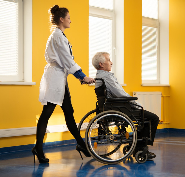 Joven enfermera alegre con hombre mayor en silla de ruedas
 - Foto, imagen