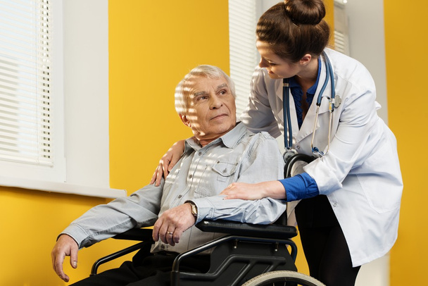 Joven enfermera alegre con hombre mayor en silla de ruedas
 - Foto, imagen