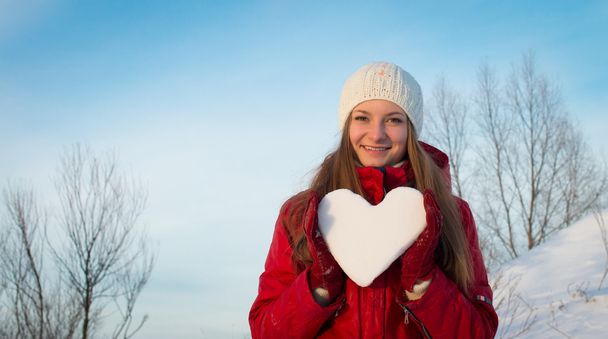 Chica sonriente con un corazón cubierto de nieve. Día de San Valentín
. - Foto, Imagen