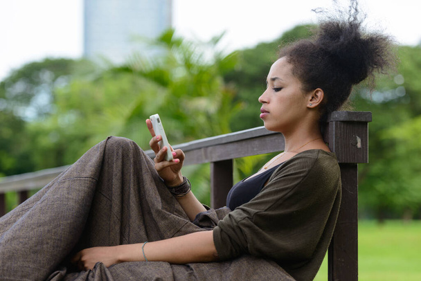 Retrato de una joven mujer africana hermosa con cabello afro relajándose en el parque al aire libre - Foto, Imagen