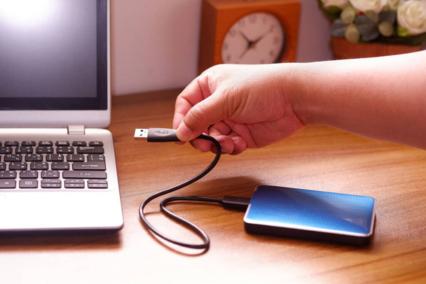 Man's hand was connecting an external portable hard disk usb 3.0 cable to laptop computer on desk, Data transfer or backup personal files concept - Photo, image