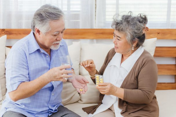 Asian couple woman caring sick elderly man by giving pill or drug at home. Love and relationship of retired senior couple. Health care and medicine of illness aged people photo concept. - Photo, Image
