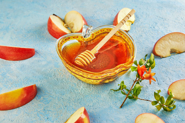 Rosch Haschana ist ein Begriff für das jüdische Neujahrsfest. Eine apfelförmige Schale mit Honig und einem Stock und einem in Scheiben geschnittenen Apfel auf blauem Hintergrund - Foto, Bild