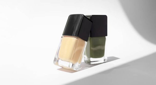 Yellow and green nail polishes glass bottles on white background with trendy hard shadows. Mockup fashion beauty products - Photo, Image
