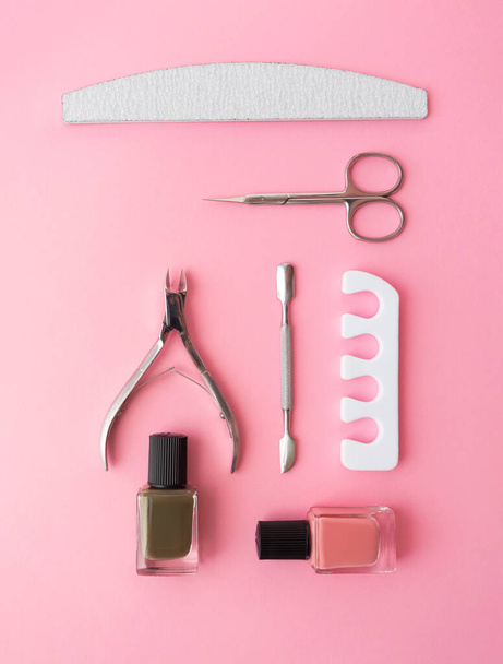 Маникюр и педикюр средства ухода за ногтями набор на розовом фоне knolling плоский лежа. Сепаратор, кутикула, папка для ногтей, кутикула, ножницы и лак для ногтей в бутылке - Фото, изображение