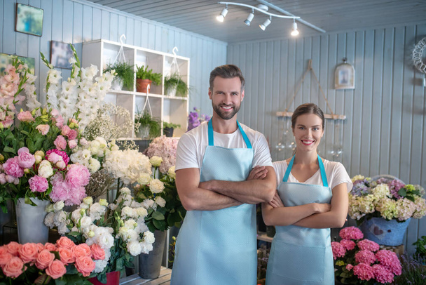 Bearded male and brown-haired female standing intside flower shop with crossed arms - Foto, Bild