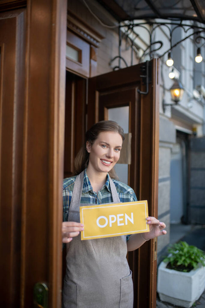 Young waitress standing at the door, holding open sign, smiling - Foto, Bild