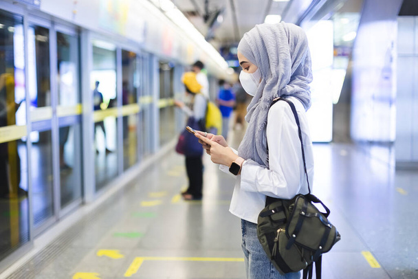 asiatico musulmano donna indossare medico faccia maschera per prevenire polvere e infezione virus, utilizzando smartphone in metropolitana treno sistema di transito pubblico. - Foto, immagini