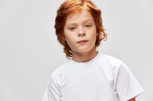 Bambino dai capelli rossi in una t-shirt bianca faccia primo piano sfondo grigio - Foto, immagini