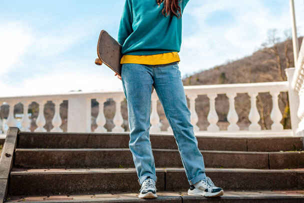 Egy fiatal tinédzser gördeszkát tart a háta mögött, a lépcsőn áll. Lényegében. Közelről. A sportéletmód és az utcai kultúra fogalma. - Fotó, kép