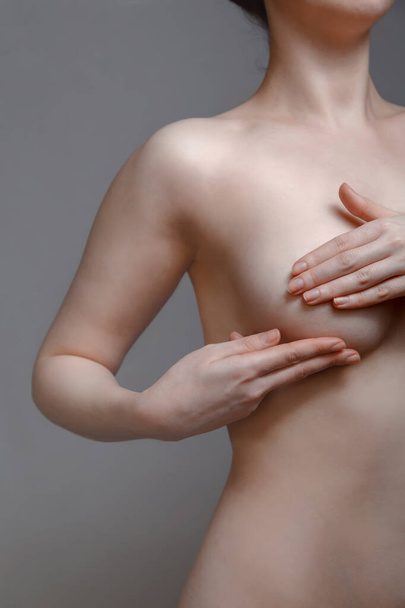 Naga młoda kobieta przeprowadza samoocenę piersi, aby zachować zdrowie kobiet. Szare tło. - Zdjęcie, obraz