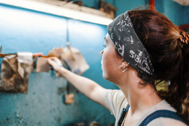Rovnost pohlaví. Portrét mladé ženy v uniformě pracující v dílně, která přikládá kus papíru se záznamem na stěně. Pozadí je rozmazané. Zavřít. - Fotografie, Obrázek