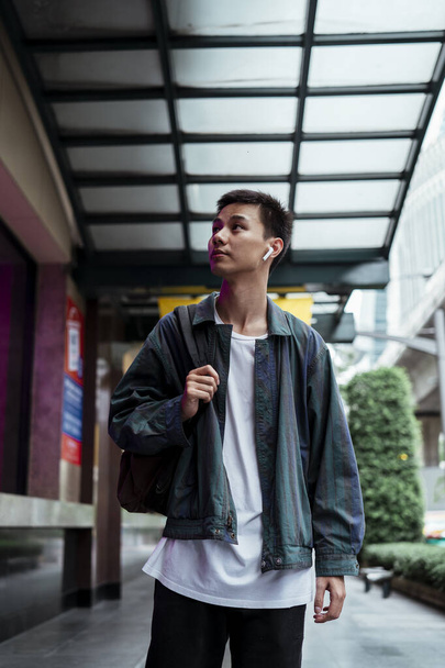 Коротке волосся хлопець в куртці носити Bluetooth навушники, що ходять по місту і озираються навколо
. - Фото, зображення