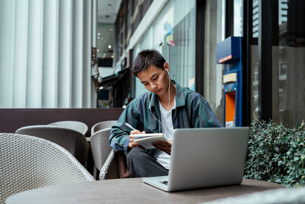 Krótkie włosy facet siedzi na tarasie kawiarni i wykonuje swoją pracę z notebooka i laptopa. - Zdjęcie, obraz