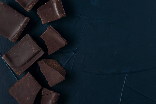 Pieces of chocolate on the dark blue textured background. Flat lay. Copy space. - Photo, Image