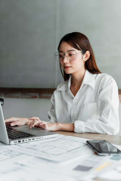 Długie włosy kobieta projektant wnętrz w białej koszuli noszenia okularów i używać CAD do pracy przy stole. - Zdjęcie, obraz