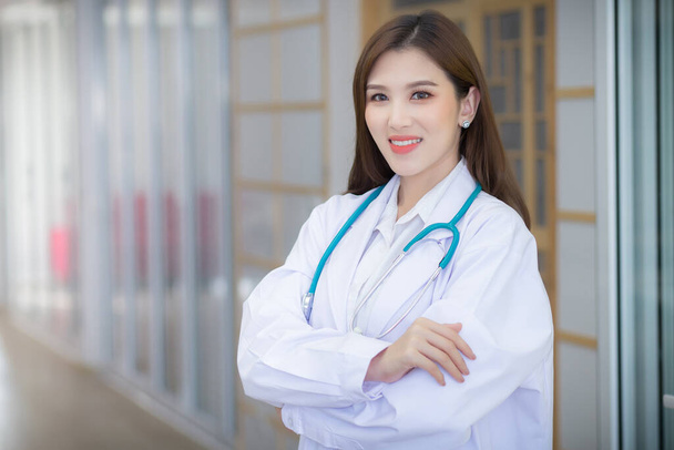 Egy ázsiai doktornő, aki keresztbe tett kézzel áll. Fehér köpenyt és sztetoszkópot visel. - Fotó, kép