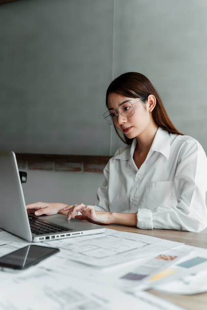 Dlouhé vlasy žena interiérová návrhářka v bílé košili nosí brýle a používat CAD pro její práci u jídelního stolu. - Fotografie, Obrázek
