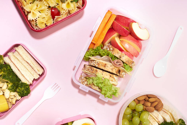 Top view pattern of school lunchboxes with various healthy nutritious meals on pink background - Foto, imagen