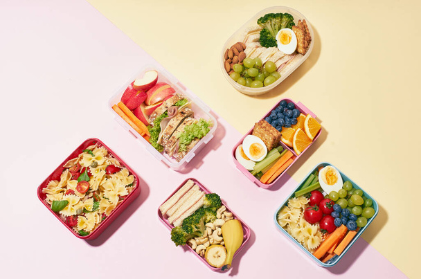 Top view pattern of school lunchboxes with various healthy nutritious meals on pink background - Фото, изображение