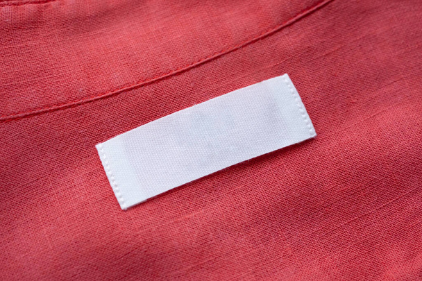 Λευκό λευκή ετικέτα ρούχα ετικέτα σε κόκκινο λινό πουκάμισο υφασμάτινη υφή φόντο - Φωτογραφία, εικόνα