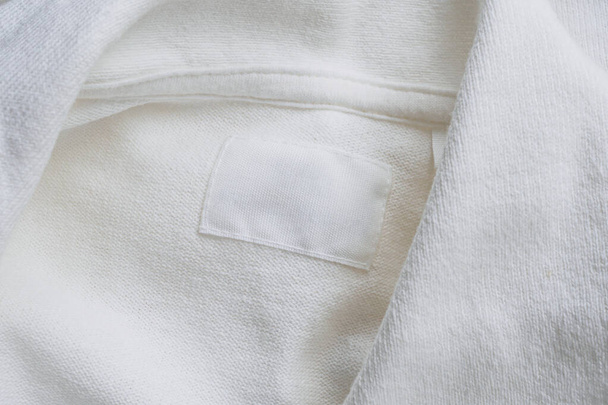 Blanco witte kleding label op nieuwe katoenen shirt achtergrond - Foto, afbeelding